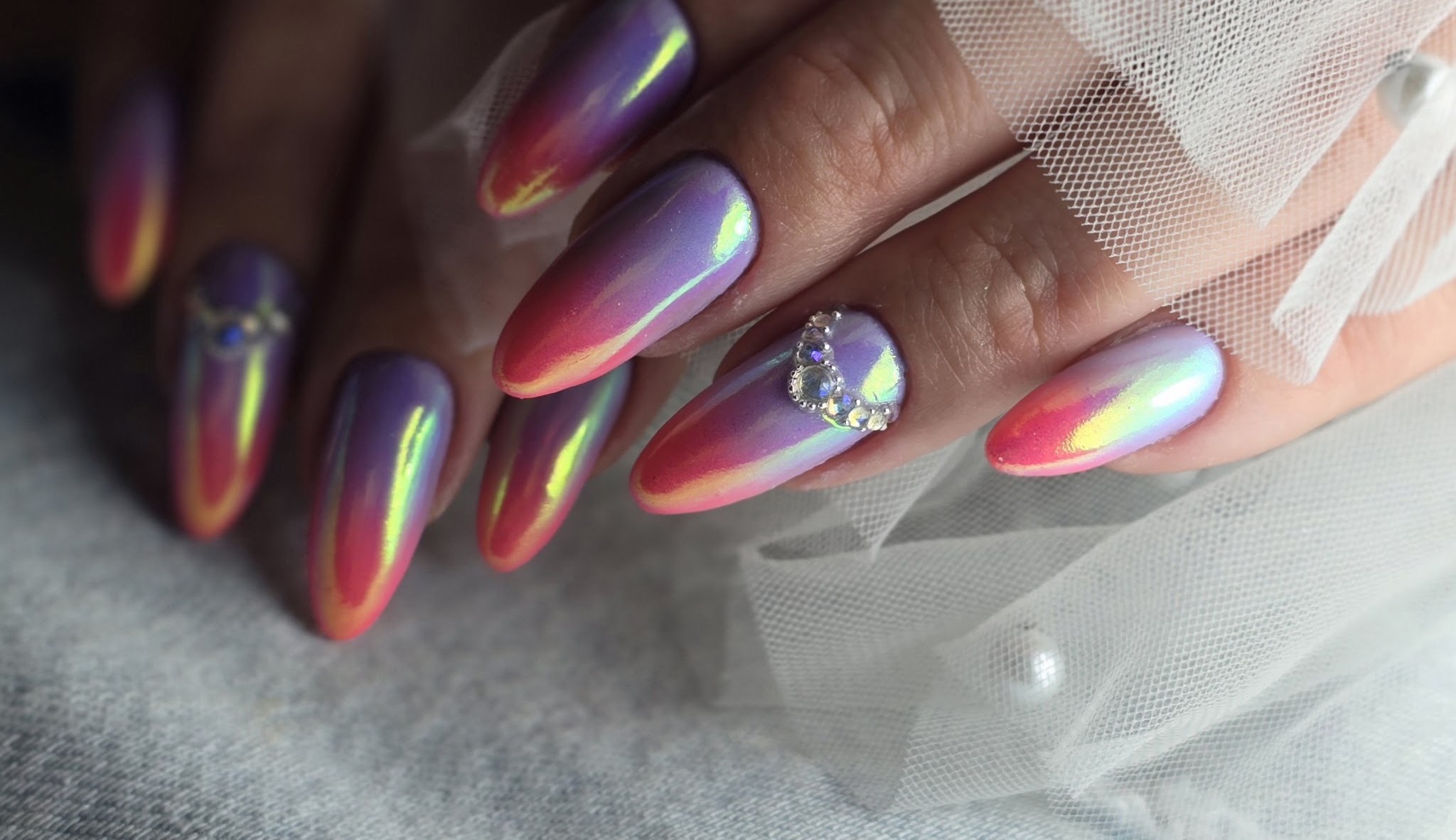 Paarse en roze chrome amandelnagels met een kristal, op witte tule